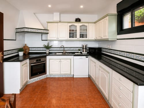 Cocina moderna en la casita Vila Santa Rita, Oia con muebles color crema, encimeras de granito negro y piso de terracota