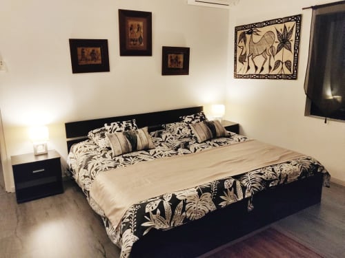 Chambre moderne avec lit à structure noire, linge de lit botanique noir et blanc, tables de nuit sombres avec lampes, inspiré africain