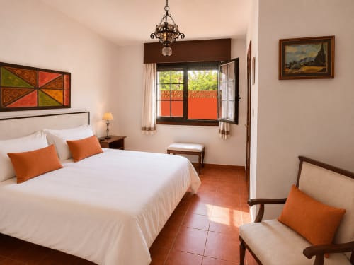 Dormitorio luminoso en Oia con ropa de cama blanca, detalles naranjas, piso de terracota y puertas de balcón con vistas al mar en Holibai