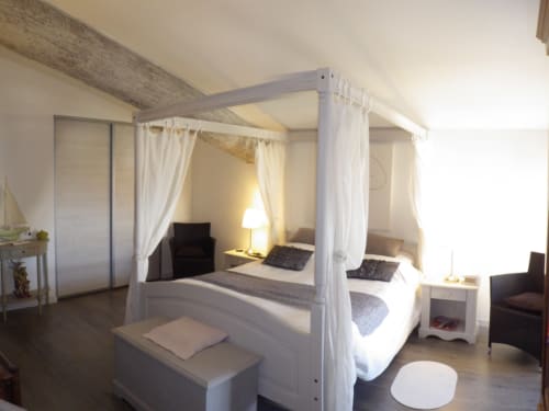Lit à baldaquin élégant dans la chambre d'une villa du XVIIIe siècle rénovée, aux rideaux blancs, poutre apparente et lumière chaleureuse à Villas Lux