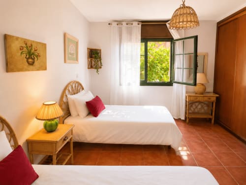 Luminoso dormitorio de cabaña en Oia con camas gemelas, muebles de madera, piso de terracota y ventana con postigos verdes