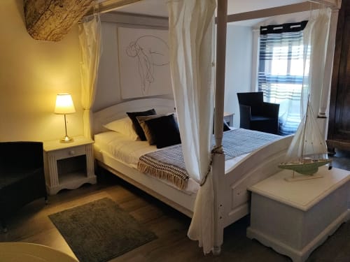 Lit à baldaquin luxueux aux voilages blancs dans la villa de Béziers, éclairage chaleureux, oreillers noirs, vue sur la piscine