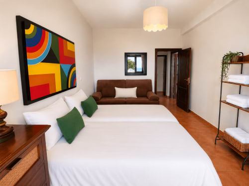 Dormitorio espacioso en la villa Santa Rita de Oia con cama queen, sofá marrón, obras de arte coloridas, pisos de madera y vista al mar