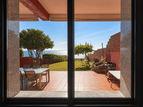 Vista desde la casita Vila Santa Rita en Oia con terraza, mesa de comedor, vistas al mar, jardín con árbol y construcción de ladrillo