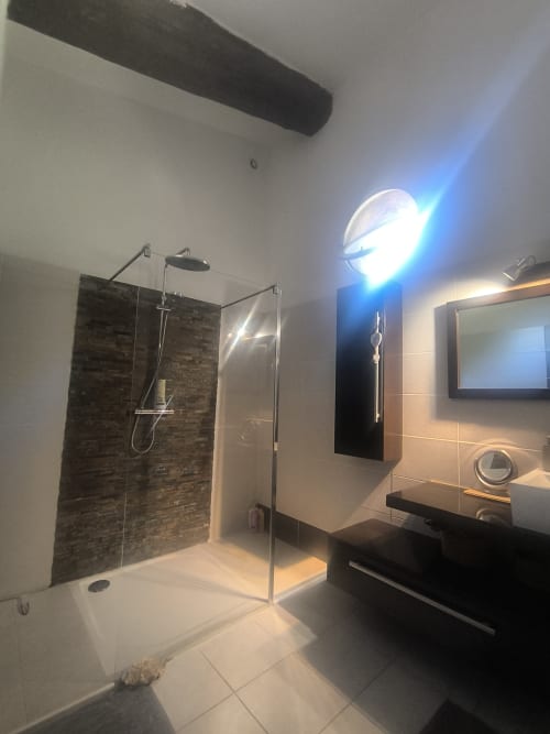 Salle de bain moderne avec douche spacieuse, carrelage noir, vanité noire, lampe chauffante et téléviseur aux Villas Lux Tropical
