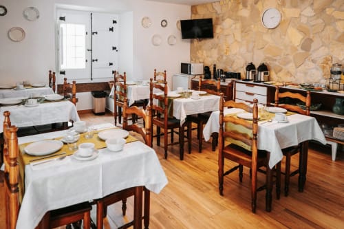Dining room at Casa de Campo da Quinta da Pegada in Óbidos with wooden tables, white tablecloths, and rustic stone accent