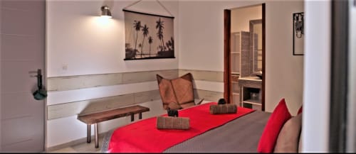 Chambre moderne aux Villas Lux Tropical avec lit aux finitions rouges, banc en bois, panneaux muraux blancs et accès à la salle de bains attenante
