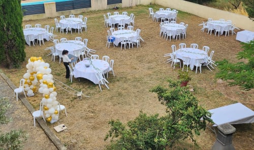 Installation d'événement en plein air au Domaine De Poulharies à Carcassonne avec tables blanches, chaises et arche de ballons dorés et blancs
