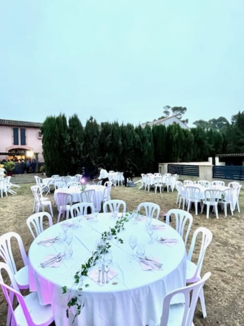 Réception de mariage en plein air au Domaine De Poulharies à Carcassonne avec tables rondes blanches, serviettes violettes et grands cyprès