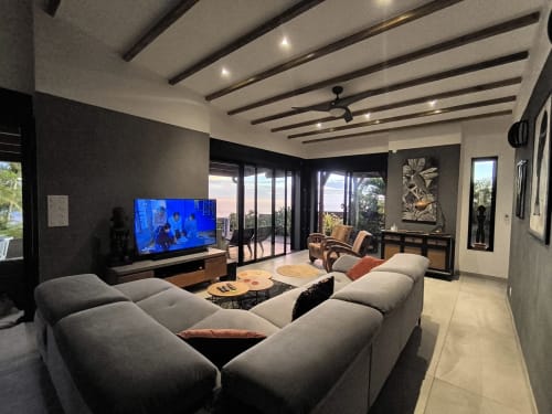 Villa moderne avec canapé gris, téléviseur, plafond à poutres et vue sur l'océan