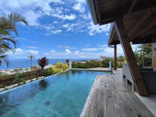 Piscine chauffée à débordement avec vue sur l'océan bleu à la Villa Lux Cap Austral, Saint-Pierre Réunion, palmiers et panorama côtier