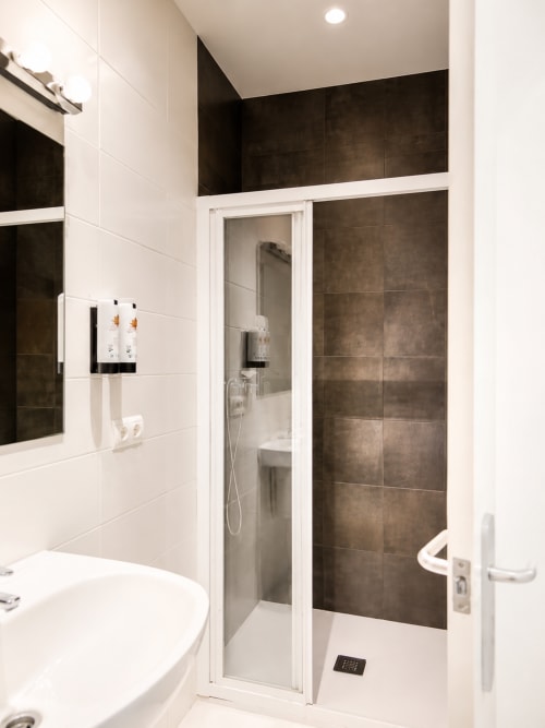 Bany modern amb rajoles blanques i gris fosc, cabina de dutxa, vàter i lavabo a l'hotel Mas Ribas de Palamós