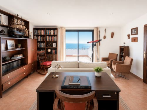 Elegante sala de estar en la cabaña Vila Santa Rita, Oia, con vista al mar, muebles de madera, librería y terraza frente al océano
