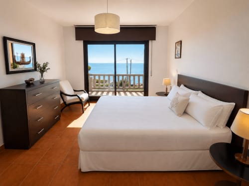 Dormitorio luminoso con balcón con vistas al mar en la casa Vila Santa Rita de Holibai en Oia, con cama doble y muebles de madera oscura
