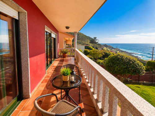 Terraza costera soleada en Vila Santa Rita en Oia con vistas al mar, patio amueblado, paredes rojas y horizonte oceánico