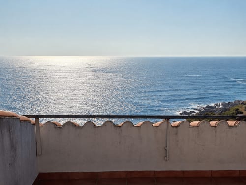 Vista al océano desde la terraza de Vila Santa Rita en Oia con mar brillante, cielo despejado y rocas costeras