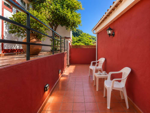 Terraza de muros rojos con sillas blancas en la villa Santa Rita de Oia, con baldosas de terracota y vistas al mar