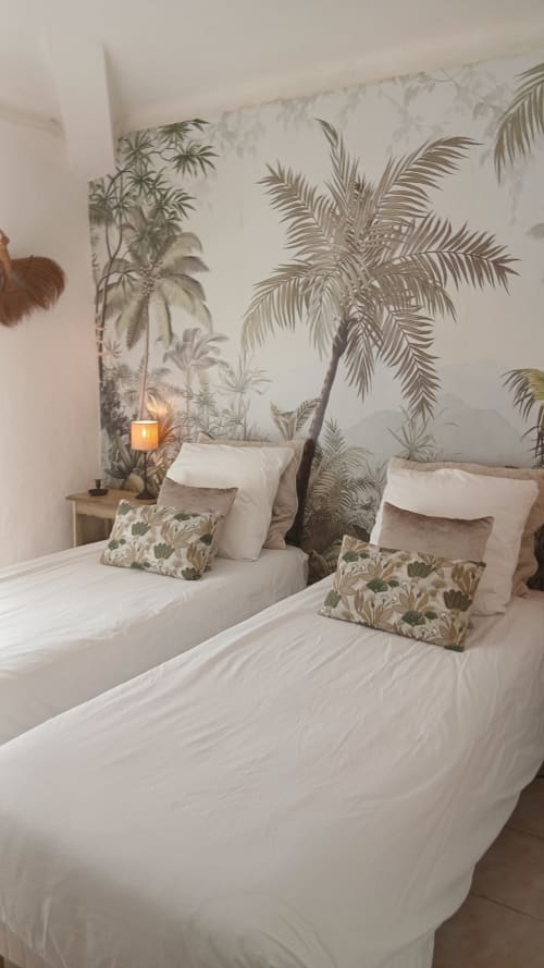 Lits jumeaux aux draps blancs et oreillers motifs devant un papier peint tropical de palmiers dans une chambre du gîte La Ribeyrette