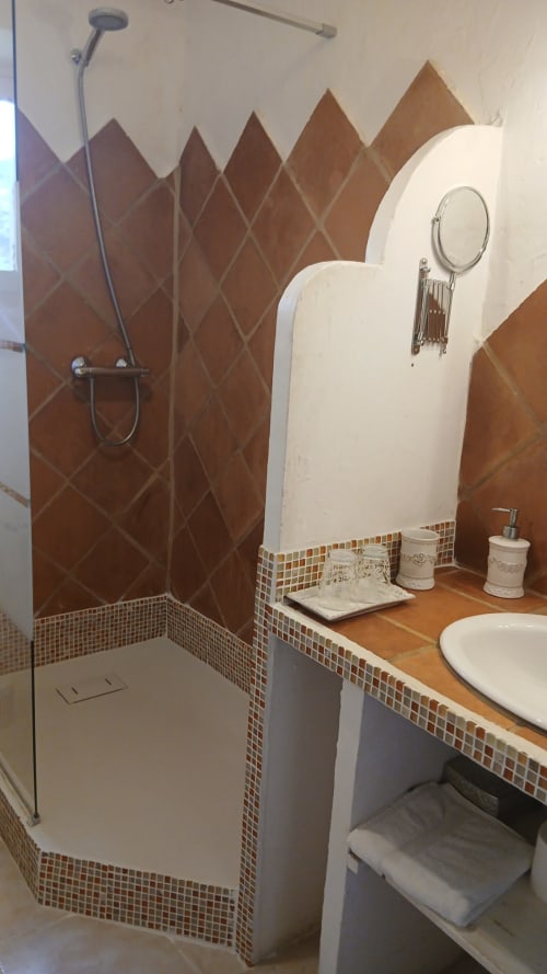 Salle de bain moderne avec douche en carrelage losange marron, lavabo blanc, sèche-serviettes chauffant et frise en mosaïque au gîte La Ribeyrette