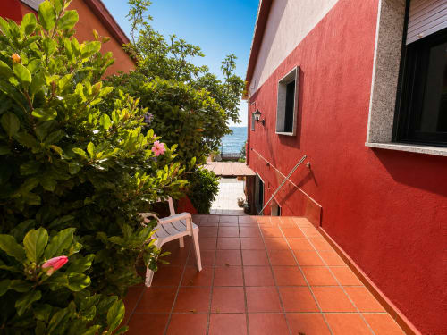 Terraza de cabaña roja en Vila Santa Rita en Oia con vista al mar, flores en macetas y asientos al aire libre