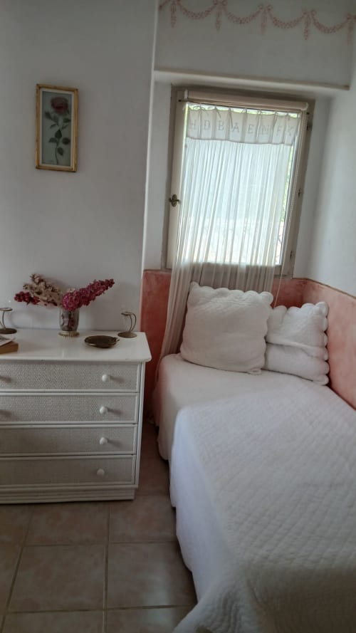 Chambre douillette au gîte La Ribeyrette avec lit à tête rose, draps blancs, table de nuit fleurie et porte donnant sur le jardin