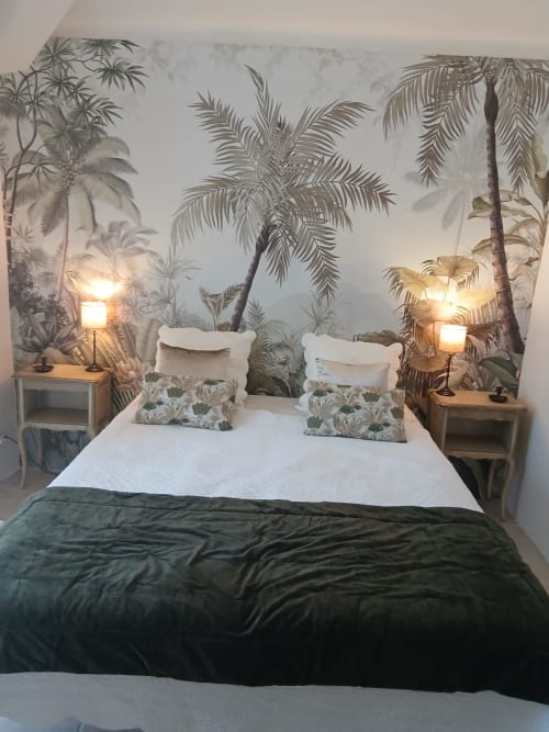 Chambre accueillante à La Ribeyrette avec papier peint tropical, literie blanche, plaid vert, lampes de chevet et vue sur le jardin