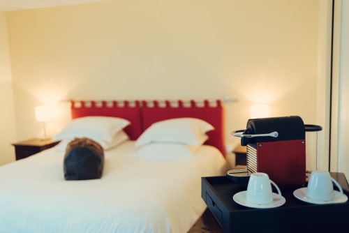 King bed with red headboard, coffee machine, and cups in Clos Céleste room overlooking pool