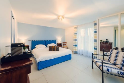 Bright bedroom with blue king bed, striped chairs, and pool view at Clos Céleste, Etretat