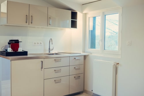 Modern beige kitchen with stainless steel sink, white cabinetry, and windows at Clos Céleste, Etretat