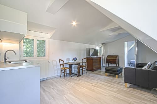 Modern junior suite with open-plan living at Clos Céleste, Etretat. White kitchen, wooden dining table, dark sofa, vaulted