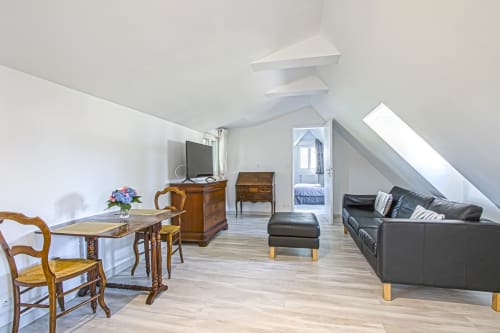 Spacious junior suite at Clos Céleste with black leather sofa, wooden furniture, and pool view through skylight in Étretat