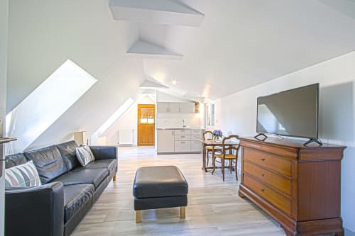 Modern attic suite at Clos Céleste with leather sofa, wooden furniture, kitchenette, and pool view in Ecrainville, France