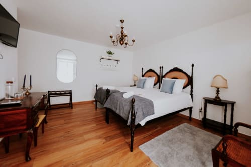 Quarto de casal elegante com cama de ferro forjado preto, assoalho de madeira e vista para o jardim na Casa de Campo da Quinta da Pegada