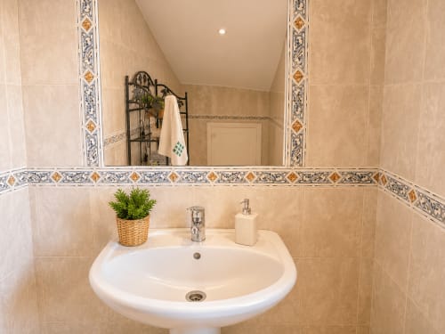 Baño elegante con lavamanos pedestal blanco, paredes de azulejos beige, cenefa decorativa y planta en maceta en Vila Santa Rita