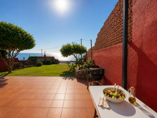 Terraza frente al mar en Oia con ensalada, villa de piedra roja, vista al mar y jardín cuidado con tumbonas