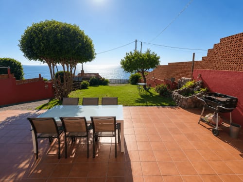 Terraza con mesa de comedor, sillas, jardín verde y vistas al mar en Vila Santa Rita, Oia