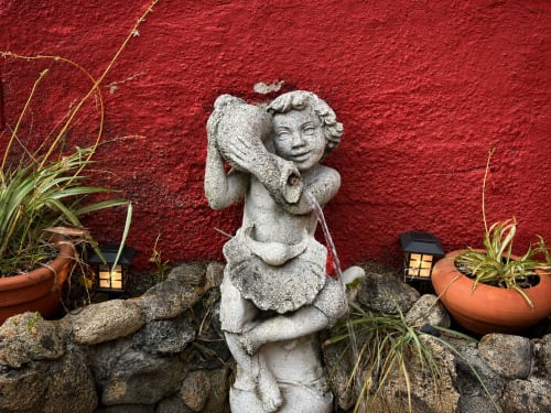 Estatua de querubín de piedra en el jardín de la villa Oia con pared roja y plantas en macetas
