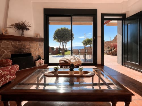Elegante sala de estar en la casa de campo Vila Santa Rita, Oia, con vistas al mar a través de grandes ventanas de marco negro, chimenea