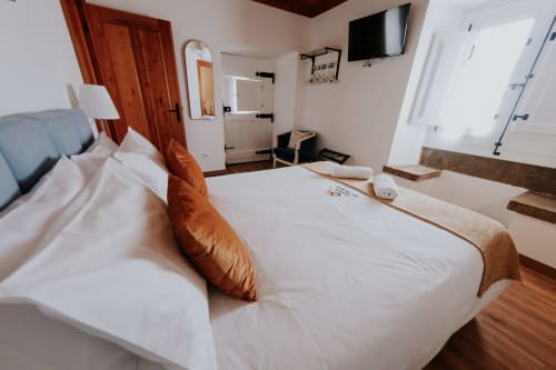 Bright bedroom at Casa de Campo da Quinta da Pegada with white bedding, orange pillow, wooden floors, and ensuite bathroom in