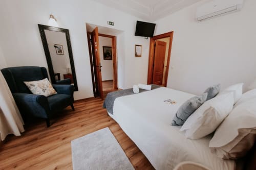 Spacious double bedroom at Casa de Campo da Quinta da Pegada with white bed, blue armchair, wooden floors, and garden view in