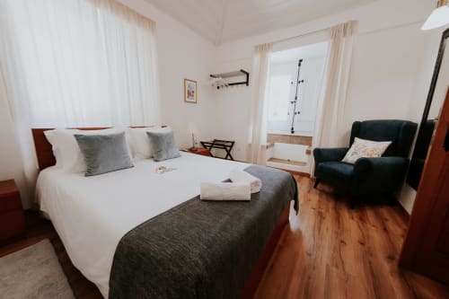 Bright bedroom in Óbidos B&B with queen bed, garden view, modern flat-screen TV, and black armchair
