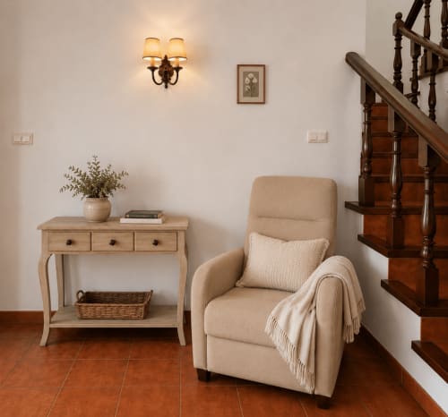 Elegante recibidor de la villa Santa Rita en Oia con sillón color crema, consola de madera y escalera de madera