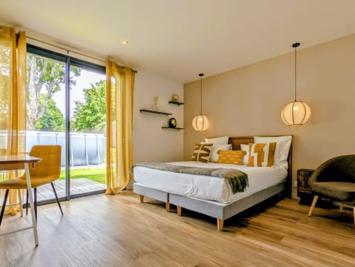 Chambre moderne à La Clairière aux Chênes avec lit, luminaires suspendus, parquet et accès à la terrasse