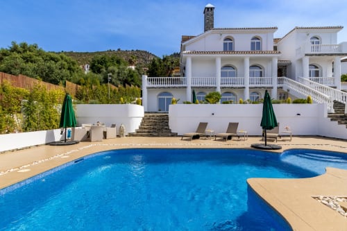 Villa de lujo blanca con piscina en Alhaurín de la Torre, vistas a la montaña, tumbonas y sombrillas verdes junto a aguas cristalinas