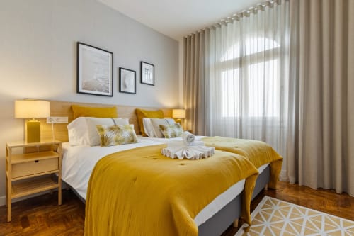 Luminoso dormitorio moderno con ropa de cama amarillo dorado, mesitas de noche de madera y grandes ventanales con vistas a las montañas en Ayma Villa