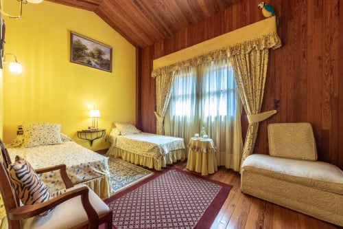 Habitación amarillo brillante en el Palacio Vasco con camas gemelas, vigas de madera, cortinas doradas y decoración tradicional