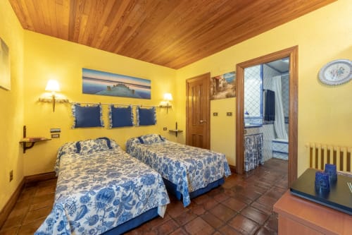 Dormitorio Apartamento Azul en Palacio Vasco con camas gemelas, paredes amarillas, techo de madera y ropa de cama floral azul en Laukariz