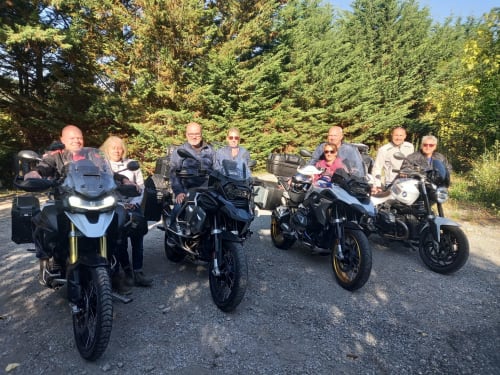Group of motorcycle riders posing together at La Méridienne in Venterol, France with forest backdrop