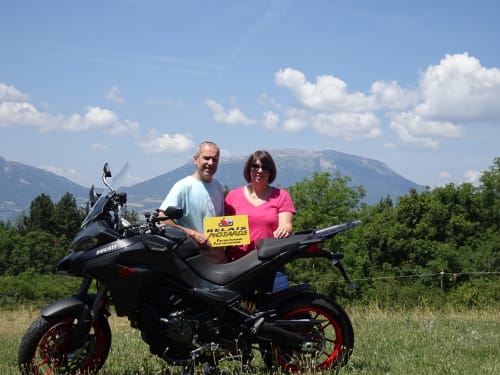 Couple with Ducati motorcycle holding La Méridienne sign, mountains in background near Venterol, France