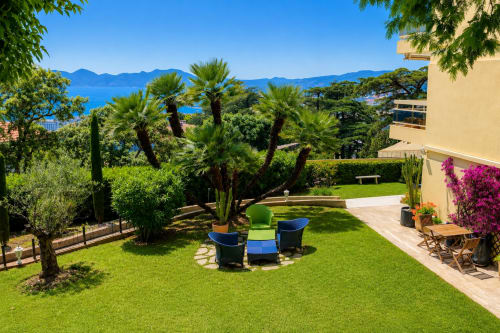 Cannes apartment garden with sea view, palm trees, loungers, and Mediterranean landscape overlooking the coast